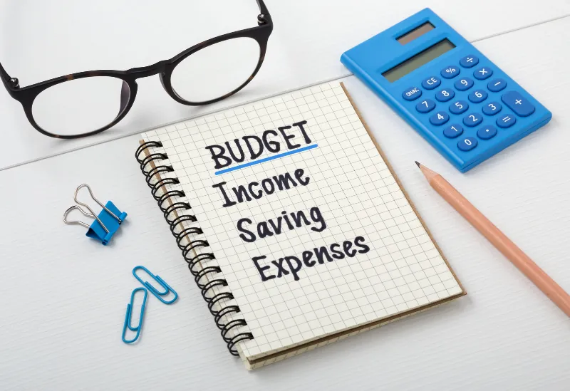 Notepad with handwritten entries for income, savings, and expenses, representing business budgeting tips for cutting costs.