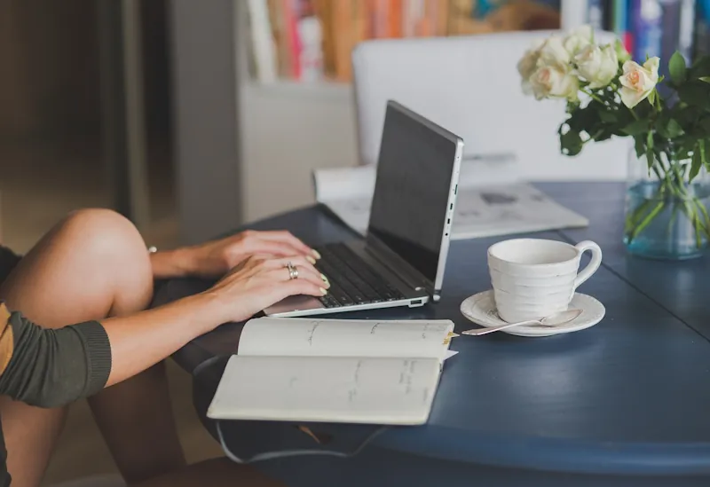 Woman using a laptop with a notebook and coffee at home