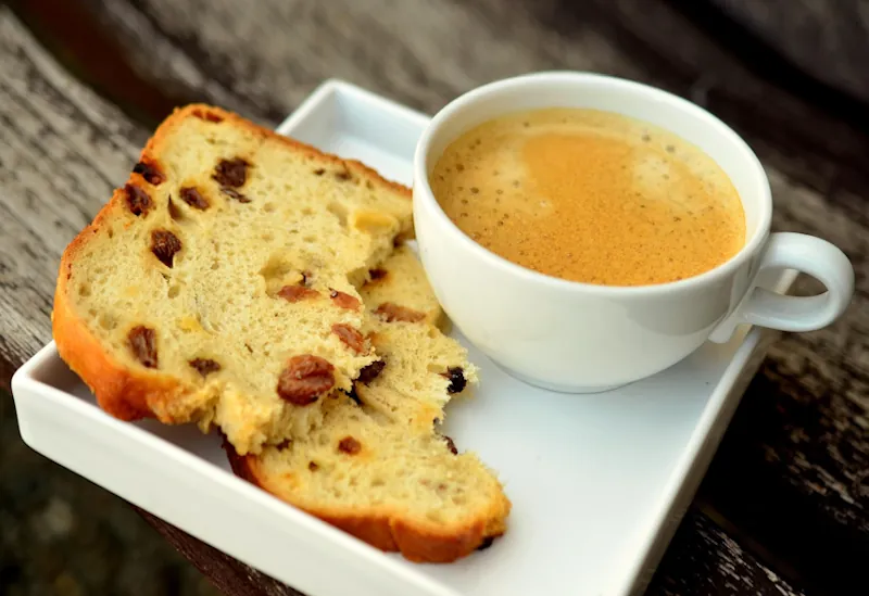 Cup of coffee on a table next to a slice of fruit cake