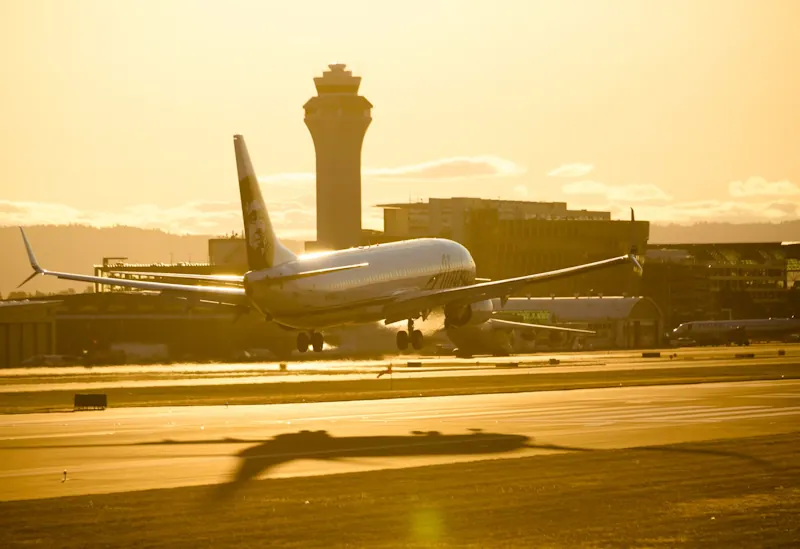 Airplane taking off at sunset with airport tower in the background, illustrating travel and flight savings.