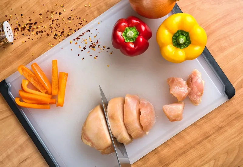 Chicken breast being sliced on a board with fresh peppers