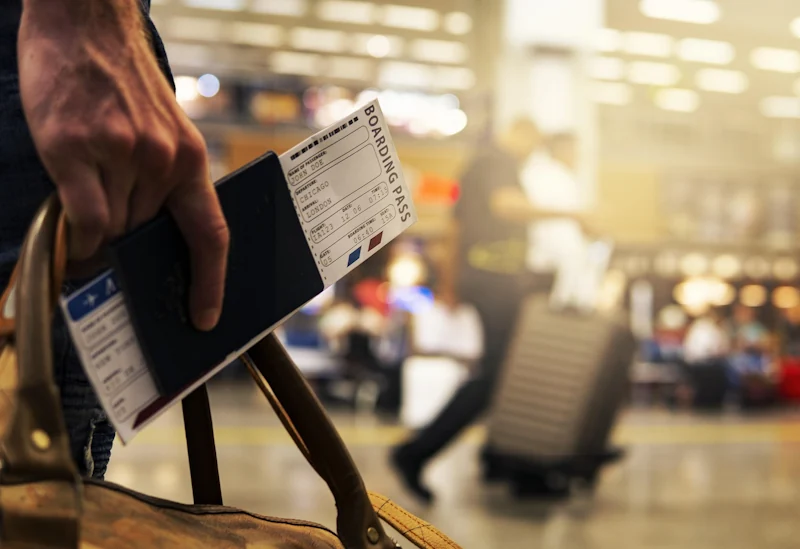 Man holding a passport, tickets and bag at an airport
