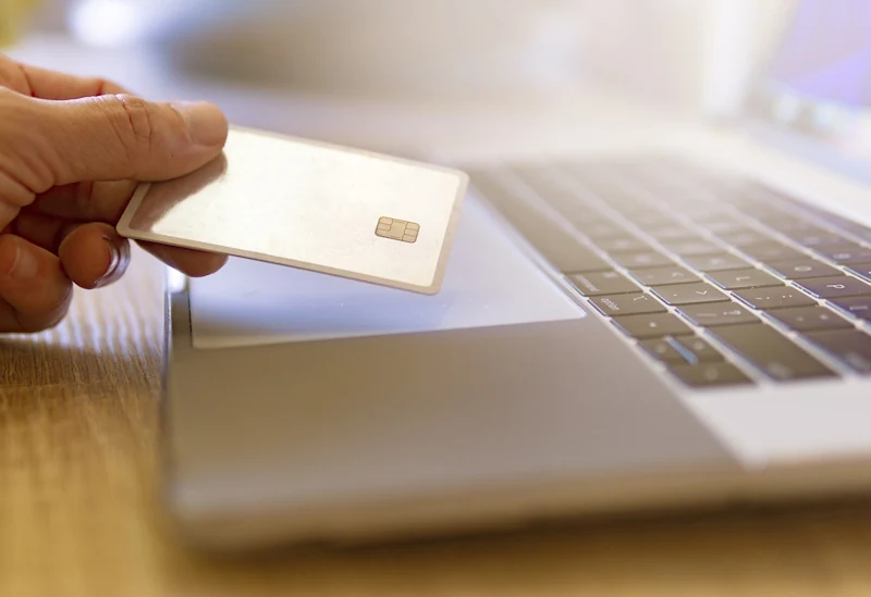 Hand holding a credit card over a laptop, representing online travel booking and discounts.