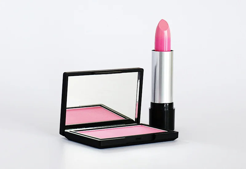 Pink lipstick standing next to a folding mirror on a light surface