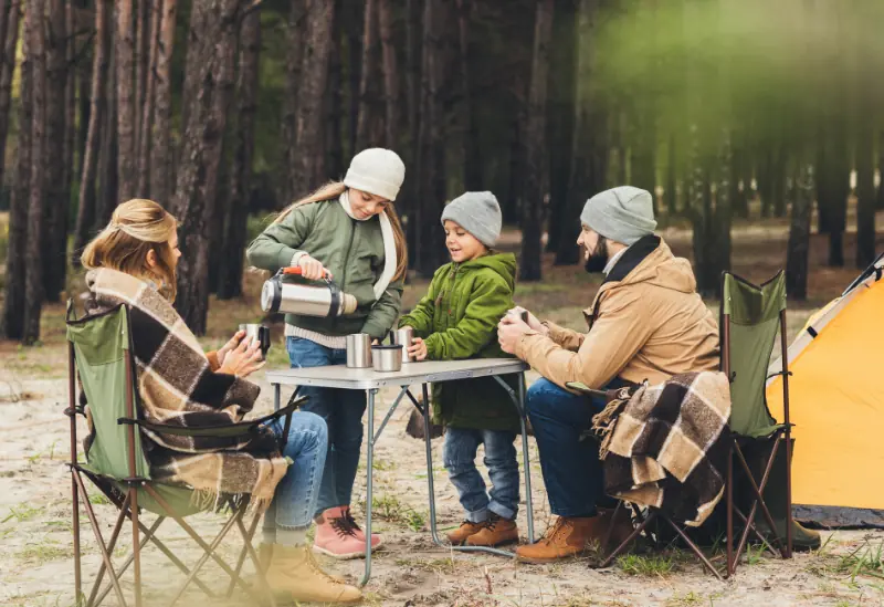 Family setting up a camping tent with backpacks and sleeping bags on a weekend outdoor trip