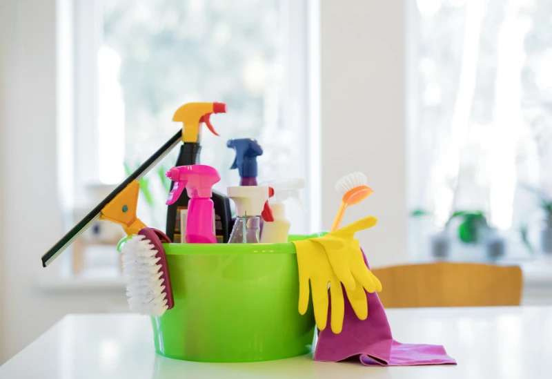 A bucket filled with assorted household cleaning products like sprays, cloths, and sponges.