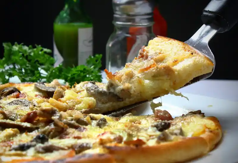 Slice of mushroom and ham pizza being lifted from the pan with a drink in the background