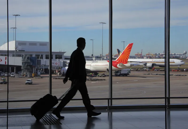 Silhouette of a man with a small suitcase walking through airport gates with planes outside