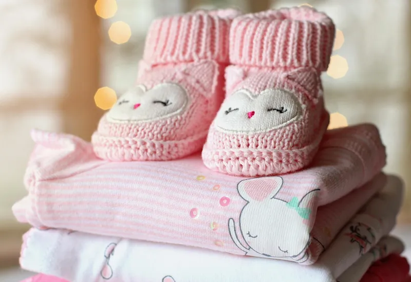 Pink baby clothes folded with crochet booties on top