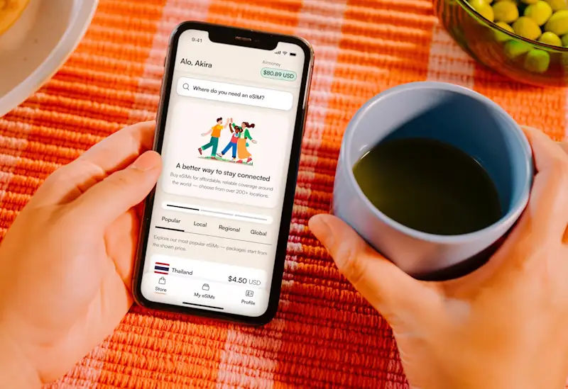 Person holding a phone while viewing eSIM plans, with a coffee in hand.