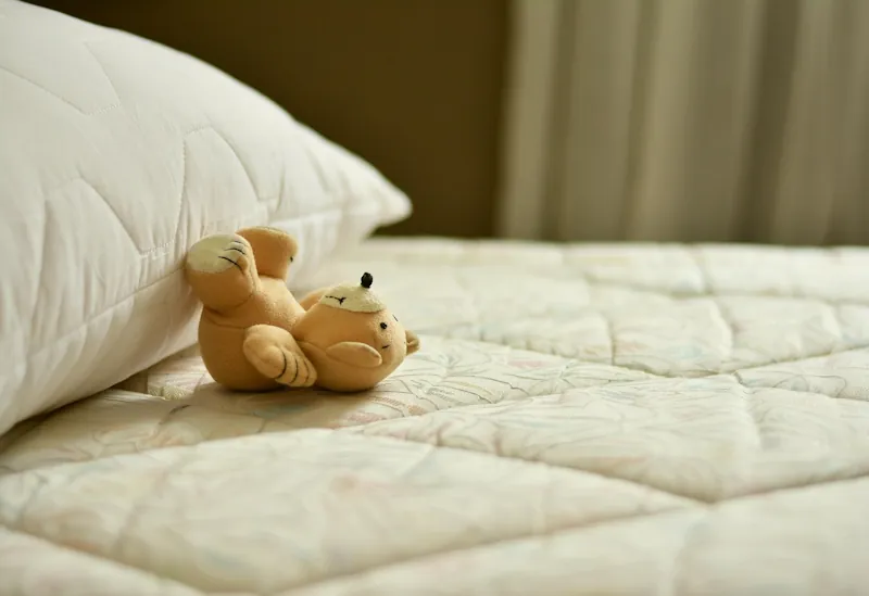 White mattress and pillow with a small teddy bear on the bed