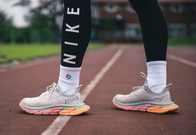 Person running on track wearing white leggings and Hoka trainers