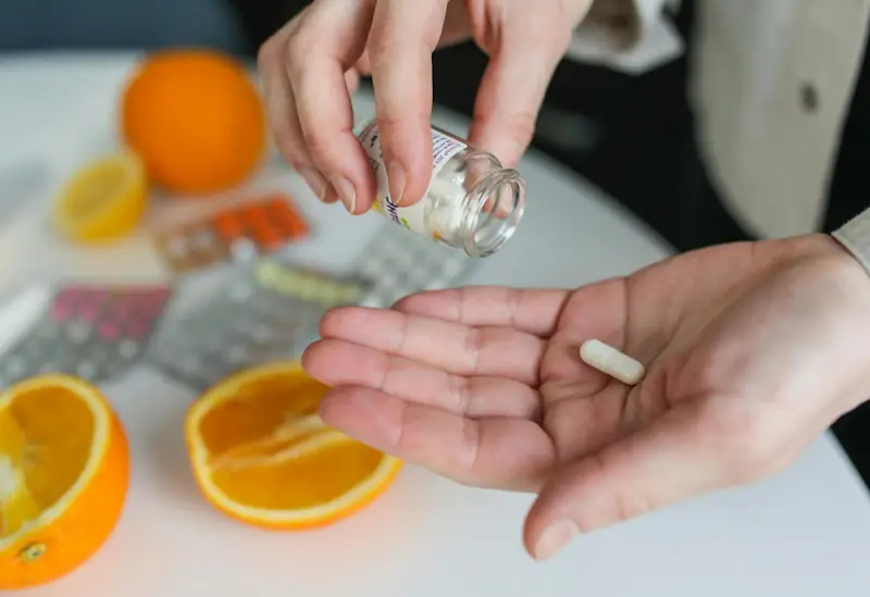 Person holding a tablet from a glass bottle on a table with sliced oranges