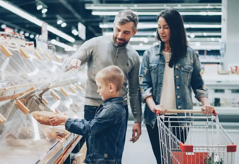 Family choosing bread in a supermarket, representing everyday grocery shopping costs.