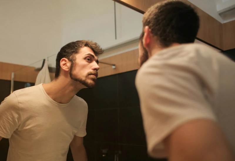 Young man checking his appearance in the mirror as part of his looksmaxxing softmaxxing routine