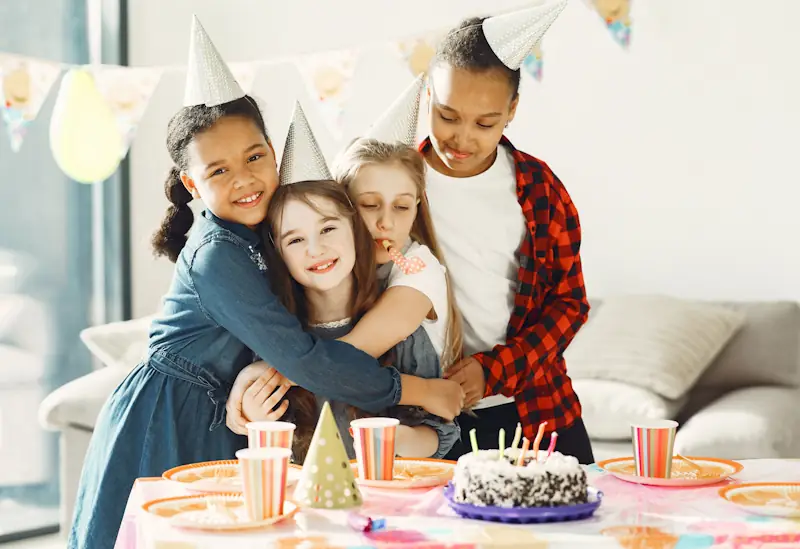 Children celebrating a birthday party around a table with cake and decorations.