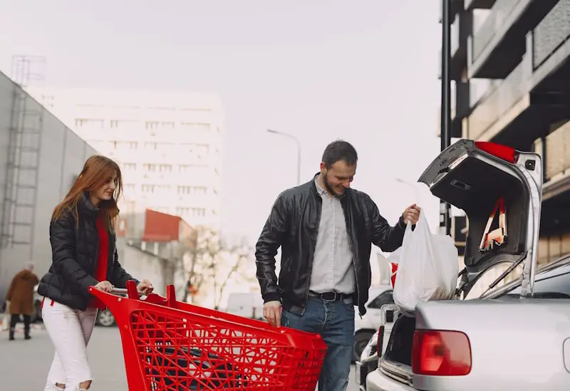 Person loading grocery bags into a car boot in a supermarket car park.