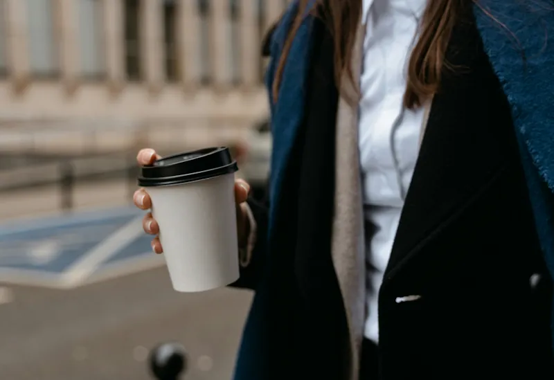 Person holding a takeaway coffee cup while walking outdoors.