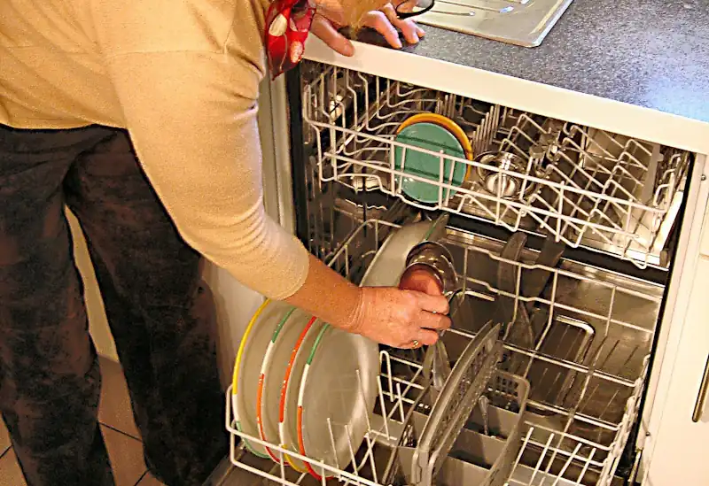 Person loading dishes into a dishwasher in a kitchen.