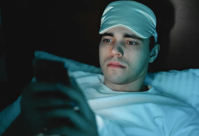 Person looking at their phone in bed late at night with the screen lighting their face.