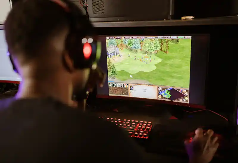 Person playing a video game at a computer desk with headphones on.