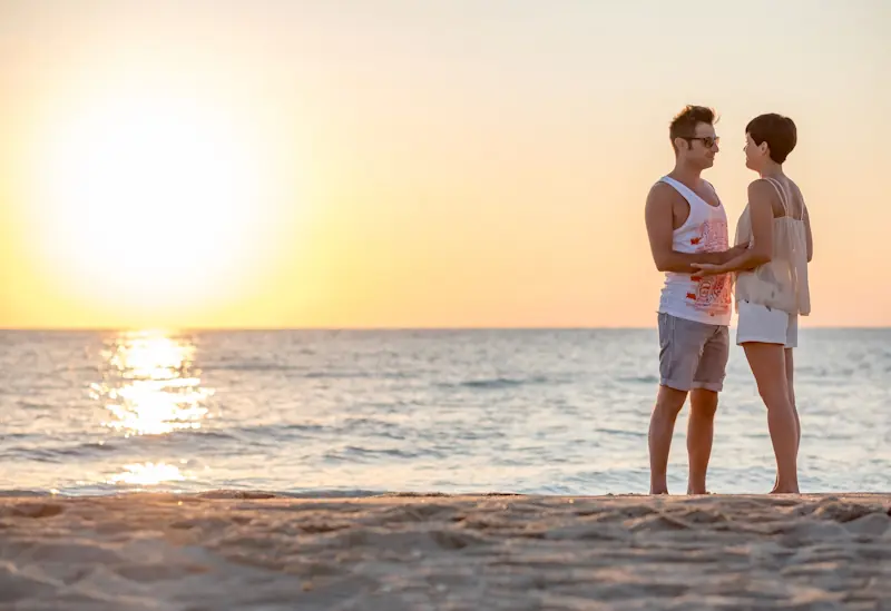 Couple holding hands on a beach at sunset.