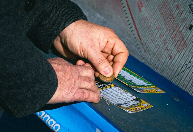 Person scratching a lottery ticket with a coin.