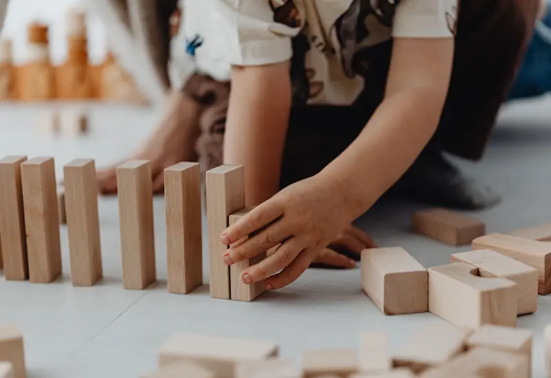 Toddler playing with wooden blocks on the floor in a bright nursery setting.