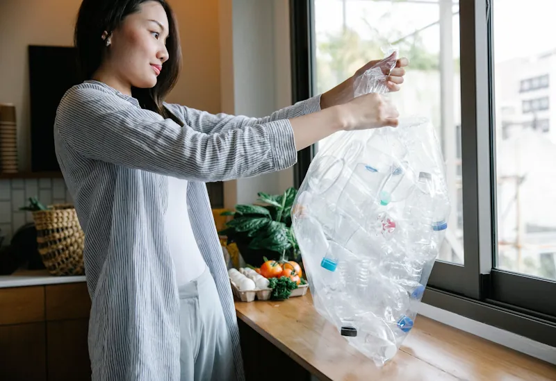 Person holding a bag of empty plastic bottles in a kitchen.