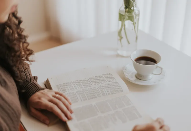 An open Bible on a table with a cup of coffee nearby.