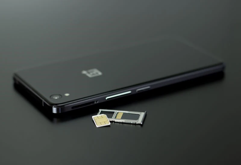 Smartphone with a SIM card and SIM tray on a dark surface.