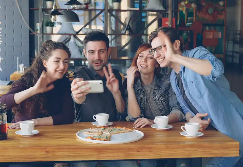 Friends taking a selfie together at a café table with pizza and coffee.