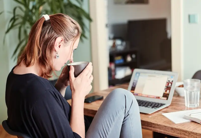 Person holding a mug of tea while working at a desk.
