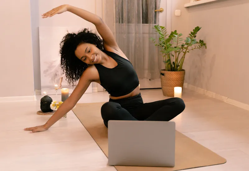 Person doing a yoga stretch at home with a laptop open in front of them.