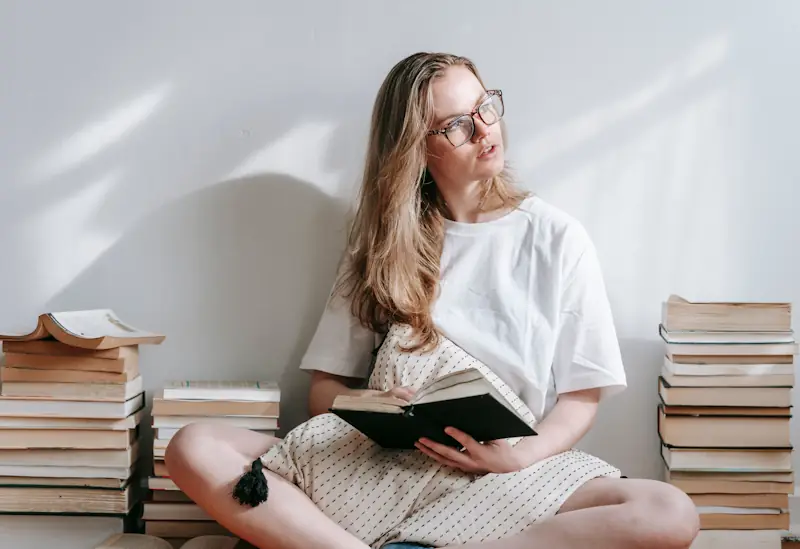 A person reading a book while sitting on the floor between stacks of books