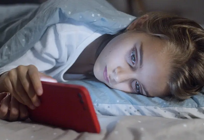 A person lying in bed at night holding a smartphone close to their face