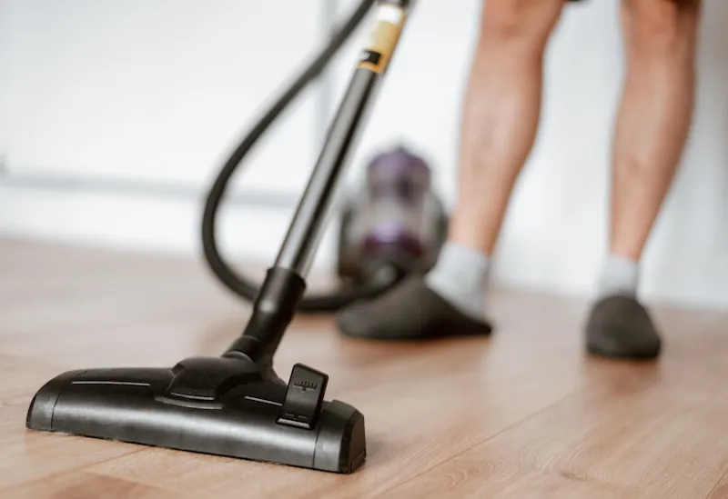 A person vacuuming a wooden floor in a tidy home