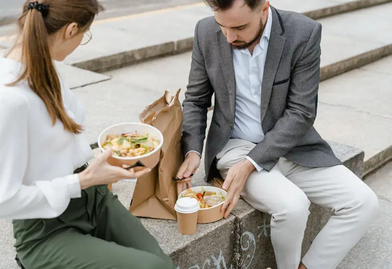 Two people eating takeaway food on outdoor steps during a casual lunch break