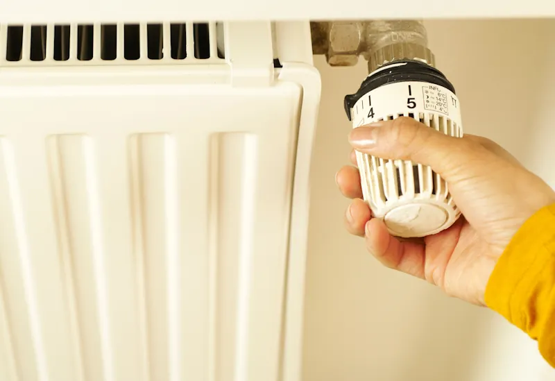 A hand adjusting the temperature dial on a household radiator