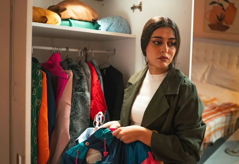 A person standing in front of an open wardrobe holding several clothing options