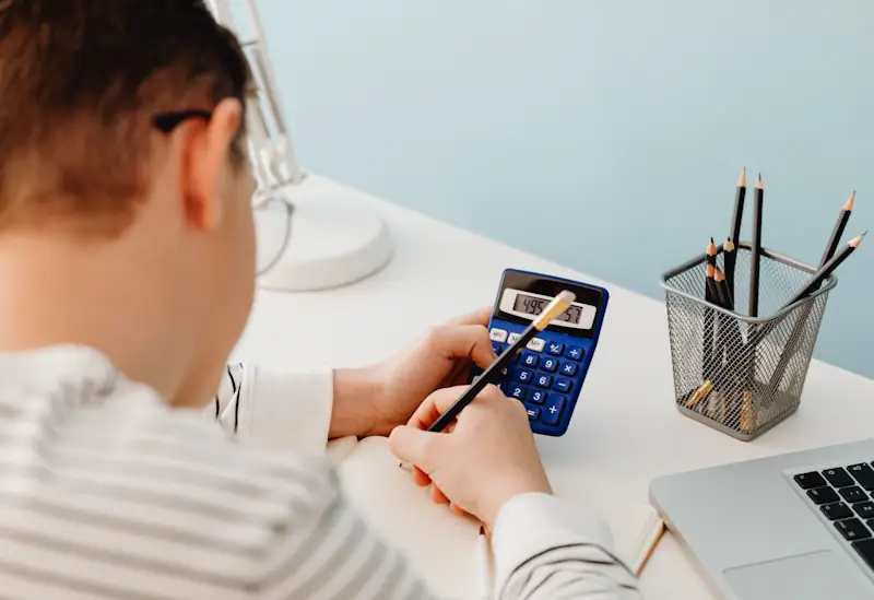 A person sitting at a desk using a calculator and writing in a notebook