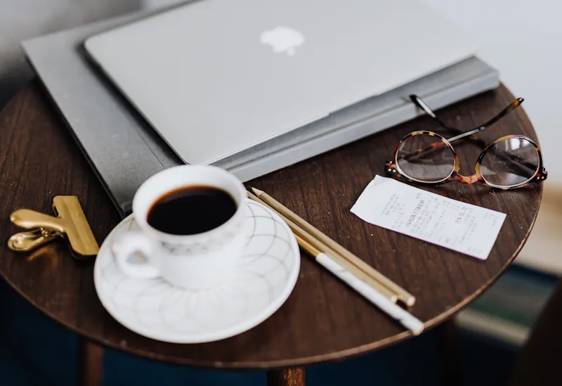 Coffee, receipts and a laptop on a small table, symbolising everyday habits that quietly increase monthly spending.
