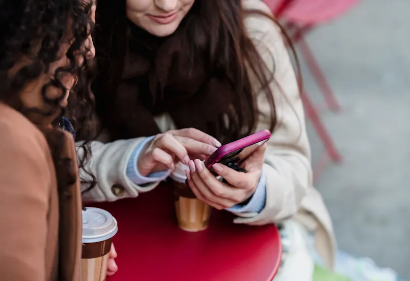 Two people holding takeaway coffees while looking at a smartphone, representing everyday habits that quietly cost money.