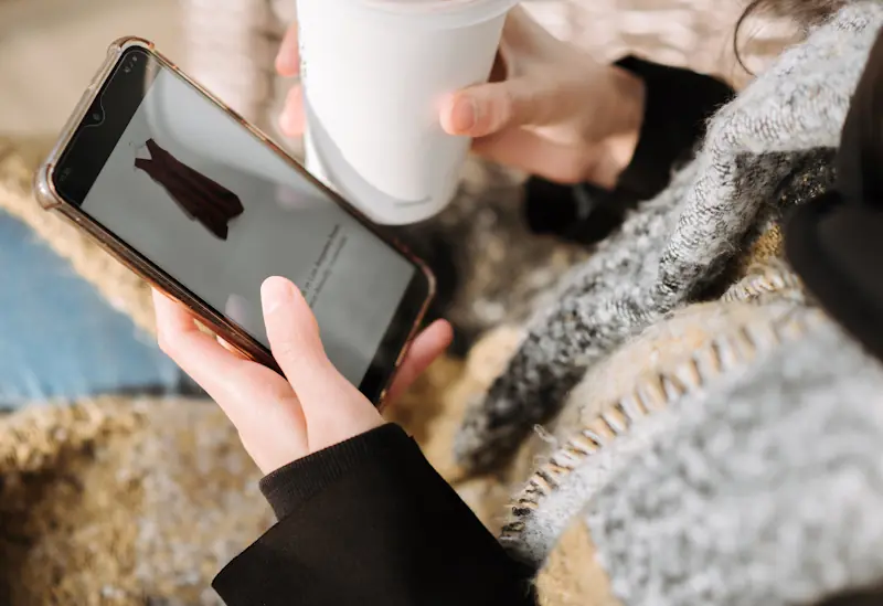 Person browsing an online shopping page while holding a takeaway drink, representing everyday decisions that quietly waste money.