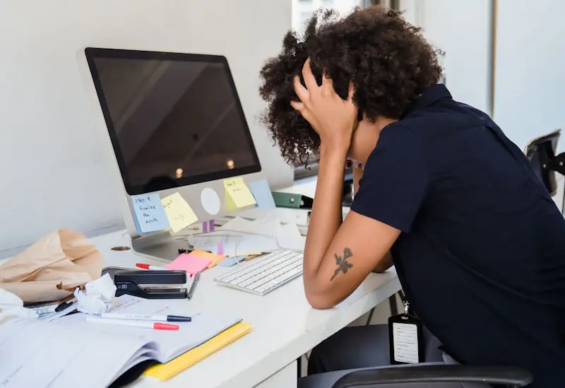 A person reviewing documents at a desk with a laptop, printed papers, and a crumpled sheet of paper