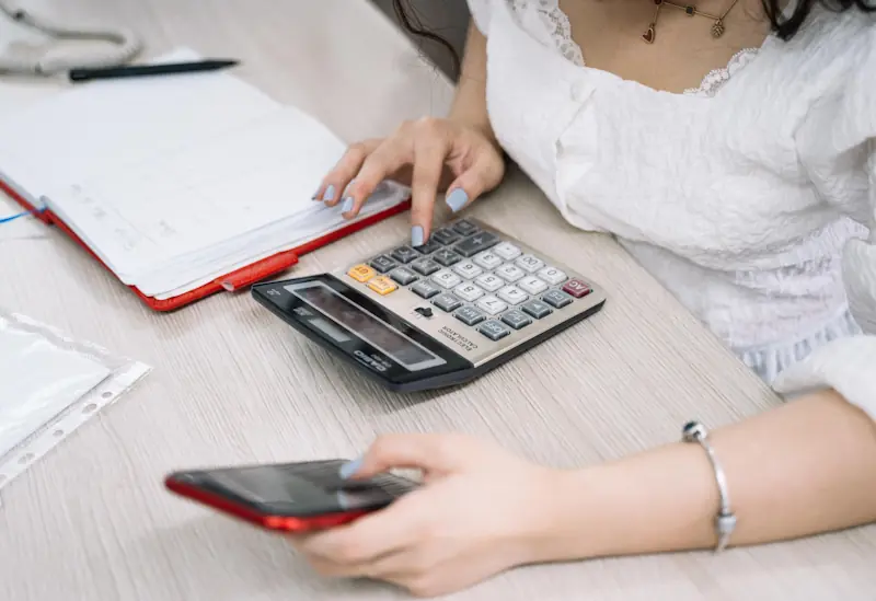 Person using a calculator, smartphone and notebook to track financial habits and improve daily money routines.