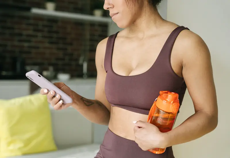 Person in activewear holding a water bottle and smartphone, representing healthy living habits on a budget.