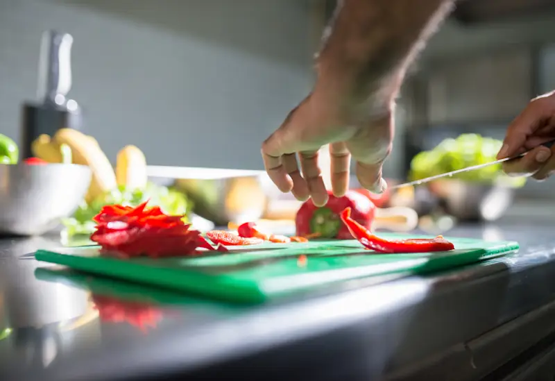Fresh vegetables being sliced on a kitchen cutting board in natural light