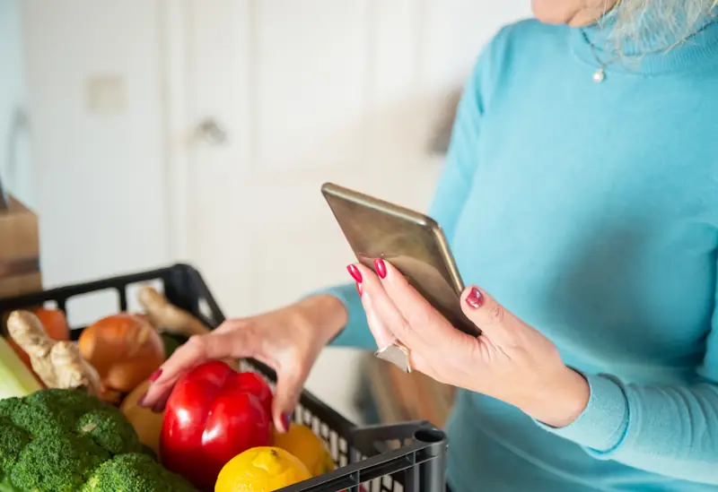 Person checking their phone while sorting groceries, representing how to build a monthly budget that actually works.