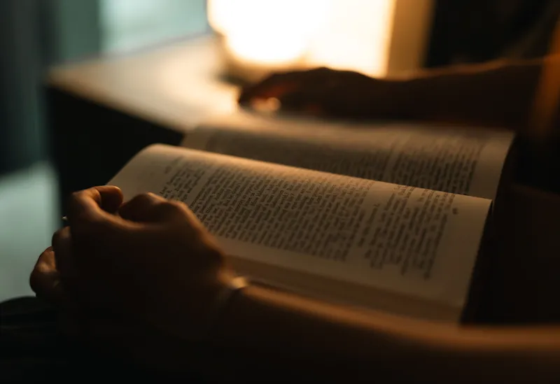A person reading an open book under warm ambient lamp light